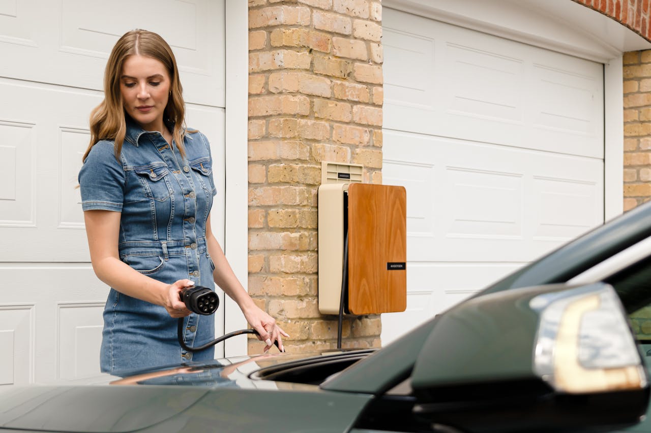 our-story A woman plugs in an electric vehicle charger at a home charging station.